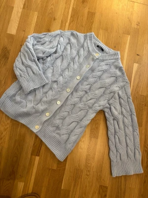Ljusblå kabelstickad kofta Gina Tricot - Ljusblå kabelstickad kofta från Gina Tricot med stora vita knappar framtill. Koftan har ribbade muddar vid ärmslut och nederkant samt en rund halsringning. Perfekt för lager på lager och ger en chill vibe till din outfit.Gina Tricot chunky cardigan in size M. It's only been washed once and is in like-new condition as I’ve never actually worn it.