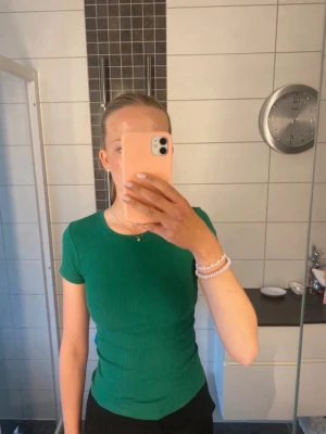 Grön ribbad topp från FB Sister - Säljer en grön ribbad topp från FB Sister. Den har en tight passform, korta ärmar och rund halsringning. Perfekt för dig som gillar en enkel och stilren look. Materialet är mjukt och stretchigt, vilket gör den bekväm att bära.