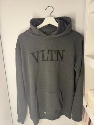 Mörkgrå VLTN hoodie - Snygg mörkgrå hoodie från Valentino med VLTN-logga broderad på bröstet. Klassisk passform med huva och känguruficka framtill. Tillverkad i mjukt bomullsmaterial som känns skönt mot huden. Perfekt för en avslappnad och trendig look.