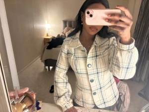 Vit och blå rutmönstrad cardiganjacka - Säljer en snygg cardiganjacka med vit bas och blå rutmönster. Jackan har stora blå knappar framtill, klassisk krage och långa ärmar med lätt puff. Materialet ser ut att vara stickat och jackan har en avslappnad passform som är perfekt för lager.