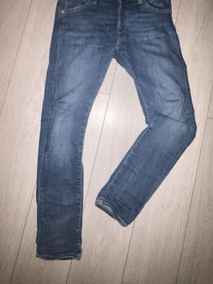 Blå slim fit jeans from Jack & Jones - Säljer ett par klassiska blå slim fit jeans med fem fickor och snygga slitningar. Jeansen har normal midja och raka ben, tillverkade i denim med stretch för extra komfort. Perfekta för dig som gillar en enkel och stilren look.