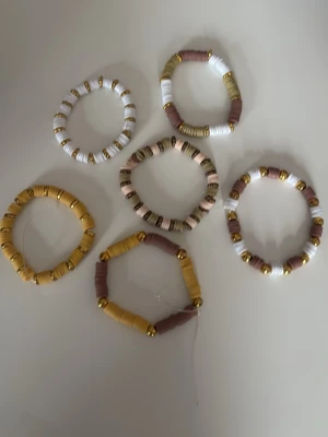 Set med färgglada pärlarmband - Säljer ett set med sex elastiska armband gjorda av pärlor i vitt, guld, beige och brunt. Armbanden har en mix av runda och platta pärlor i plast och metall-look, och passar perfekt för att ge din outfit en trendig touch. en för 15 kr alla för 90 kr