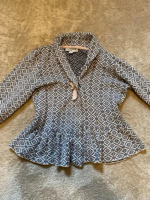 Mönstrad kofta från Mywear 146-152 - Säljer en svartvit kofta från Mywear med snyggt grafiskt mönster och volang nedtill. Koftan har hög krage och långa ärmar. Perfekt för dig som gillar unika detaljer och vill sticka ut lite extra.