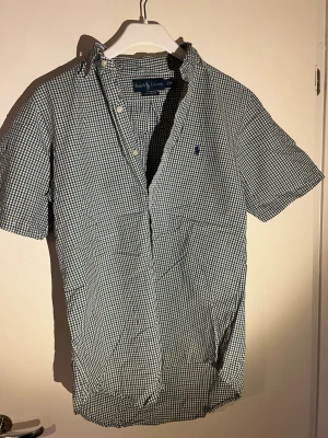 Rutig kortärmad skjorta Ralph Lauren changes - Kortärmad skjorta från Ralph Lauren i klassiskt rutigt mönster i blått och vitt. Skjortan har button-down krage, knappar framtill och en liten broderad logga på bröstet.PIKÉ-känsla i bomull som passar perfekt till sommaren.