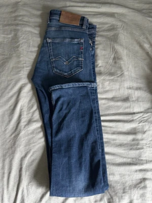 Blå jeans från Replay - Snygga blå jeans från Replay med klassisk femficksdesign och kontrastsömmar. Jeansen har en normal passform och är tillverkade i denim med en lätt tvättad look. Perfekta för en avslappnad stil.