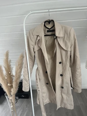 Beige trenchcoat från Zara woman  - Stilren beige trenchcoat från Zara Basic med dubbelknäppning, klassisk krage och bälte i midjan. Jackan har små defekter men inget man lägger märke till🙃