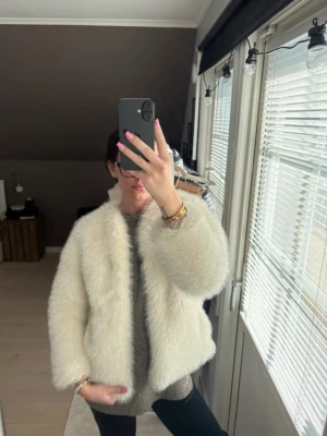 Vit pälsjacka från Zara - Säljer en fluffig vit pälsjacka från Zara med glansiga detaljer. Jackan har en kort och boxig passform, rund halsringning och är tillverkad i syntetmaterial. Perfekt för att ge din outfit en lyxig touch.