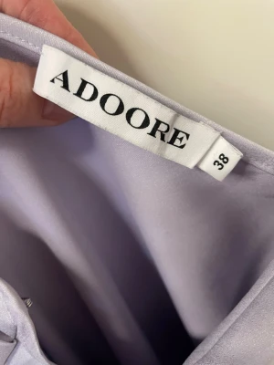 Ljuslila satin klänning från Adoore - Supersnygg ljuslila klänning från Adoore i satin med rynkade axelband och figurnära passform. Klänningen har en v-ringad överdel och är ärmlös, perfekt för dig som vill sticka ut med en elegant look.