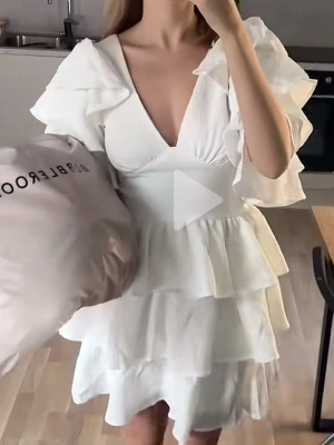 Vit volangklänning med v-ringning - Supersöt vit klänning med djup v-ringning och flera lager volanger. Klänningen har korta, vida ärmar och en figurnära passform upptill. Perfekt för dig som vill ha en romantisk och trendig look.