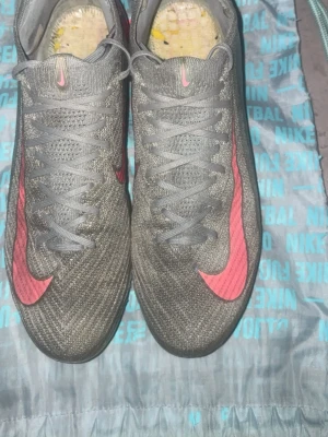 Nike Mercurial grå/rosa fotbollsskor - Säljer ett par Nike Mercurial fotbollsskor. De är använda rätt mycket men har inga öppningar. Titta på Bilden, det är lite som sticker upp från tyget men inga öppningar. Köpta för 2990kr från unisport. De är används i cirka 6 månader. Jag är öppen för byten i storlek 42 eller 26cm elite modeller.