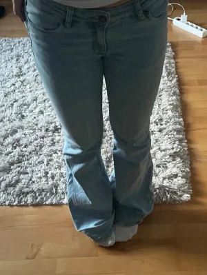 Ljusblå bootcut jeans - Säljer ett par ljusblå bootcut jeans med klassisk femficksdesign och låg midja. Jeansen har utsvängda ben och är tillverkade i denim med en lätt tvättad look. Perfekta för en avslappnad och trendig stil.