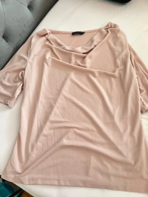 Ljusbeige topp från Stockh LM - Säljer en ljusbeige topp från Stockh LM med draperad halsringning och korta ärmar. Toppen har en mjuk och följsam känsla, perfekt för dig som gillar stilrena plagg med en twist. Passar till många olika looks och är enkel att matcha.