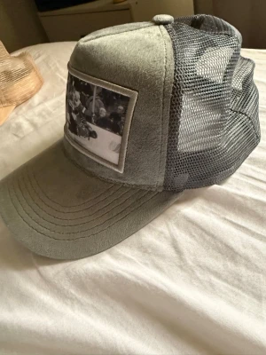 Grå mesh tiaris keps med hockeymotiv - Säljer en deppt grå keps från Tiaris med mjuk mockaliknande framsida och svart mesh baktill. På fronten sitter en  patch med svartvit hockeybild. Justerbar snapback för perfekt passform. Perfekt för dig som gillar sportig streetstyle.