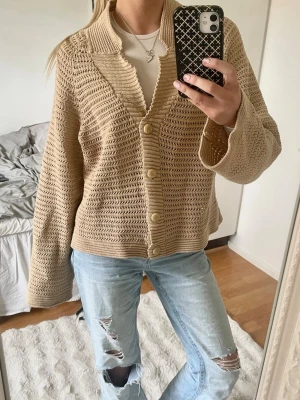 Beige virkad kofta med knappar - Snygg beige virkad kofta med stora knappar framtill och bred krage. Koftan har en avslappnad passform och långa ärmar. Perfekt att slänga över en t-shirt för en chill look.