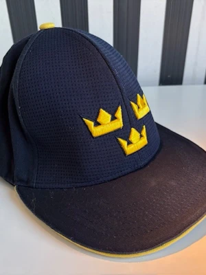 Keps, Tre kronor merch - Mörkblå keps med Tre Kronor broderat i gult på framsidan och Sweden på baksidan. Äkta officiellt Tre Kronor-merch. Endast använd vid två match-tillfällen. Bomull. OneSize