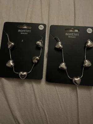 Silverfärgat hjärthalsband Montini - Säljer ett snyggt halsband från Montini med flera silverfärgade hjärtformade pärlor på en tunn kedja. Perfekt för dig som gillar stilrena och trendiga accessoarer med en touch av romantik. Materialet är metall och designen är modern och ungdomlig. Säljer 1 för 149kr och 2 för 300kr