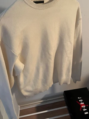 Beige stickad tröja med rund hals - En stilren beige stickad tröja med rund halsringning och ribbade muddar vid ärmslut och nederkant. Tröjan har en avslappnad passform och är perfekt för lager-på-lager. Passar till det mesta och är enkel att matcha.