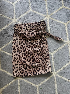 Leopardmönstrad kortkjol med knyt - Säljer en cool kortkjol med leopardmönster och knytband i midjan. Kjolen har en beige bas med mörka och bruna fläckar som ger ett trendigt och edgy uttryck. Perfekt för dig som vill sticka ut och gillar djurmönster.