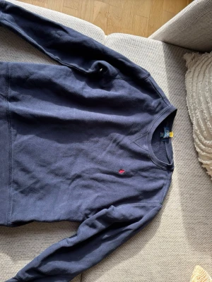 Mörkblå sweatshirt från Polo Ralph Lauren - Klassisk mörkblå <b>crewneck sweatshirt</b> från Polo Ralph Lauren med den ikoniska röda logotypen broderad på bröstet. Tröjan har rund halsringning, långa ärmar och ribb Timing vid ärmslut och nederkant. Perfekt för en avslappnad och stilren look.