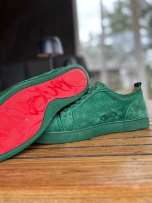 Christian Louboutin  - Snygga gröna sneakers i mocka från Christian Louboutin med klassisk låg siluett och ikonisk röd sula...? Skorna har matchande gröna skosnören och diskreta detaljer på sidan. Perfekta för dig som vill sticka ut med stil.
