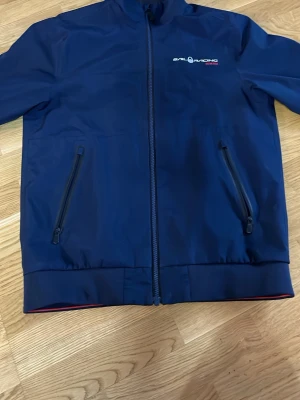 Sail Racing Gore-Tex Jacka - Snygg marinblå vindjacka från Sail Racing med GORE-TEX-material. Jackan har två snedställda fickor med dragkedja, hög krage och diskret logga på bröstet. Perfekt för blåsiga dagar och sportig stil. Pris kan diskuteras 