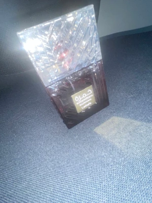 Khamrah Dukhoon Eau de Parfum - Khamrah Dukhoon Eau de Parfum från Lattafa i en elegant, fyrkantig flaska med genomskinligt mönstrat lock och mörkröd glasbotten. Flaskan har en lyxig känsla och arabiska detaljer på etiketten. Perfekt för dig som gillar orientaliska dofter.