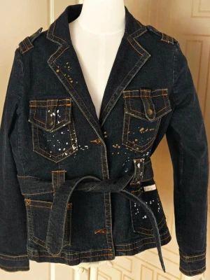 Baby Phat ÄKTA-Jeans Jacket-Y2K Gold Metallic Paint Splattered Stl XL, liten stl  - Obs! Liten stl, tajt modell i armarna Retro- Vintage! Köpt år 2006-2007 från USA  Äkta Baby Phat vara, Stl XL   Jacka total längd 60cm Armhåla till Armhåla   Design Kimora Lee Simmons Baby Phat Jeans Jacket-Y2K Gold Metallic Paint Splattered Mörkblå jeans jacka med läckert Tryck. Coola Detaljer,Avtagbart Skärp Lite använd ett fåtal ggr.  