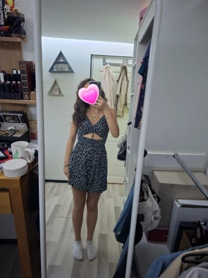 Svart blommig kort klänning - Säljer en söt svart kort klänning med vita blommor och smala axelband. Klänningen har en v-ringad urringning, cut-out detalj framtill och figurnära passform, den har också som typ shorts så den inte ska kunna blåsa upp. Perfekt för varma dagar och sommarens alla äventyr.