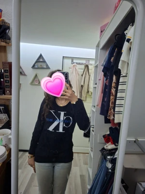 Svart Calvin Klein tröja - Säljer en snygg svart tröja från Calvin Klein med stor vit och blå CK-logga framtill. Tröjan har rund halsringning och långa ärmar. Perfekt för en avslappnad och trendig look. Tröjan har också en ficka på magen. 