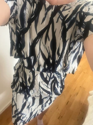 Vit och marinblå mönstrad klänning - Säljer en snygg kortklänning med abstrakt marinblått mönster på vit botten. Klänningen har korta ärmar, rund halsringning och ett avslappnat fall. Perfekt för dig som gillar unika prints och en bekväm passform.