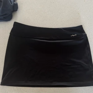 Svart kortkjol från hm  - Säljer en svart kortkjol från hm med enkel och stilren design. Kjolen har en tight passform och är gjord i ett glansigt syntetmaterial. Perfekt för dig som gillar minimalistisk stil.