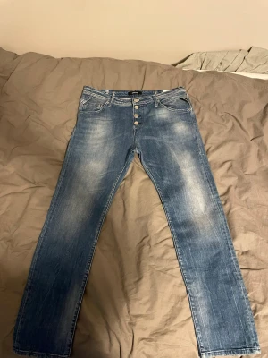 Replay jeans W29 Length 28 - Säljer ett par blå raka jeans med snygg slitning och fyra silverfärgade knappar i gylfen. Jeansen har klassiska fem fickor och kontrastsömmar. Perfekta för en avslappnad och trendig look.