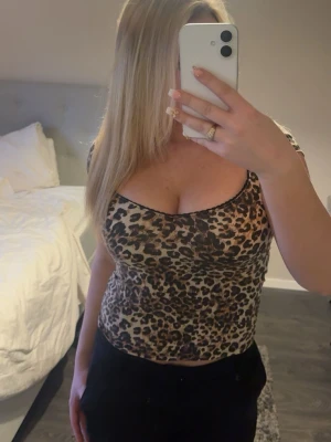 Leopardmönstrad croppad linnetopp - Snygg croppad linnetopp med leopardmönster i bruna och svarta toner. Toppen är ärmlös och har en tight passform som framhäver figuren. Perfekt för dig som vill sticka ut med ett djurmönster i garderoben.