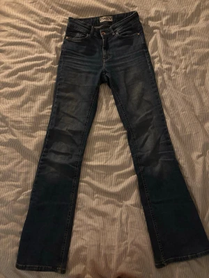 Mörkblå flared jeans från ONLY - Säljer ett par mörkblå flared jeans från ONLY med medelhög midja. Jeansen har klassisk femficksdesign och är tillverkade i stretchigt denimtyg för skön passform. Perfekta för dig som gillar 70-talsvibbar och vill ha ett par jeans som sticker ut lite extra.