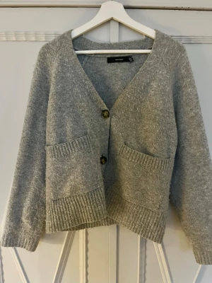 Grå stickad kofta med fickor - Super fin grå kofta med fickor framtill med bruna knappar 