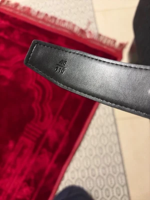 Svart bälte med ett H kommer med box  - Snyggt svart skärp i äkta skinn med stilren design och diskreta sömmar längs kanterna. Perfekt accessoar för att lyfta din outfit och funkar till många olika stilar.