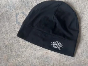 Svart mössa med vit brodyr, syna world - Säljer en svart mössa med cool vit brodyr framtill. Mössan har en enkel och stilren design med en lätt stretchig passform. Perfekt för dig som gillar streetwear och vill ha en snygg accessoar till hösten eller vintern. Central cee syna world