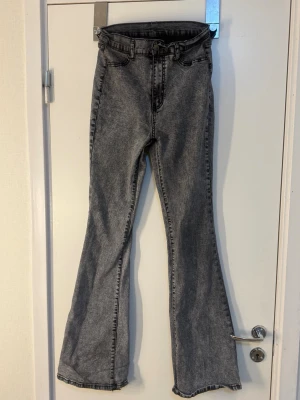 Grå bootcut jeans med hög midja - Säljer ett par grå bootcut jeans med hög midja och klassisk femficksmodell. Jeansen har en tvättad look och vida ben som slutar i en lätt utsvängd form. Perfekta för dig som gillar retrostil och vill ha ett par snygga jeans till vardagslooken.