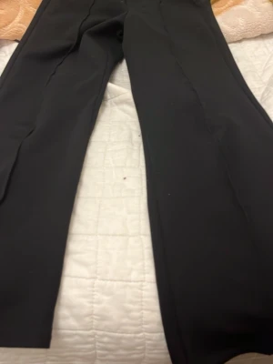 Svarta kostymbyxor från Kappahl - Stilrena svarta kostymbyxor från Kappahl med klassisk rak passform. Byxorna har pressveck framtill och är tillverkade i ett mjukt, vävt material som ger en snygg look. Perfekta för dig som vill ha en clean och enkel stil.