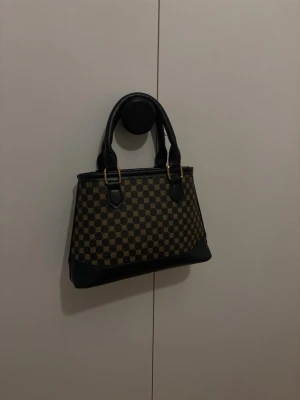 Brun handväska  - Aldrig använd och tillkommer ett långt axelband som går att knäppa på, dem klär upp outfiten med sina fina små beige mörkbruna svarta detaljer och är rymlig 