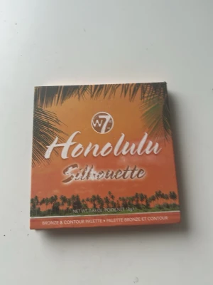 W7 Honolulu Silhouette Bronzerpalett - Snygg bronzer- och contourpalett från W7 med fyra olika nyanser i varma bruna och beige toner. Kommer i en fyrkantig förpackning med tropiskt motiv och spegel på insidan. Perfekt för att skapa solkysst look och definiera ansiktet.