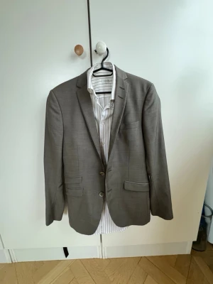 Kostympaket från Tiger of Sweden - Snygg och modern kostym i klassisk modell med två knappar framtill och två fickor med lock. Färgen är olivgrön.  Kavajen har smal passform och är tillverkad i ett tunt, vävt material som ger en stilren look. Perfekt att matcha med skjorta för en clean outfit. Perfekt till nästa fest eller kanske studenten? Kostymen kostade 5000 kr när den köptes för ca 1 år sedan och skjortan för 900 kr 