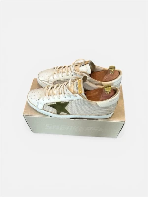 Golden Goose vita sneakers med stjärna - Snygga vita sneakers från Golden Goose med olivgrön stjärna på sidan och gulddetaljer på plösen. Skorna har vita skosnören och är tillverkade i läder och textil. Klassisk låg modell som passar till många stilar.  Kan gå ner pris! Hör av er vid intresse! 