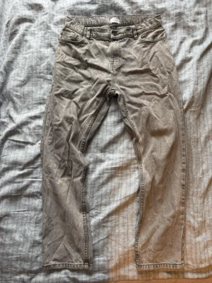 Grå jeans från Grunt - Säljer ett par grå jeans från Grunt med rak passform och klassisk femficksdesign. Jeansen har knappgylf och är tillverkade i bomulll. Perfekta för en avslappnad och stilren look. Köpte jeansen från Kids brand store