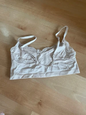 Ljusbeige bralette med spetskant. S - Söt ljusbeige bralette med tunna axelband och dekorativ spetskant längs urringningen. Mjuk och stretchig modell utan bygel, perfekt för en avslappnad look. Materialet känns lent mot huden och ger en bekväm passform.