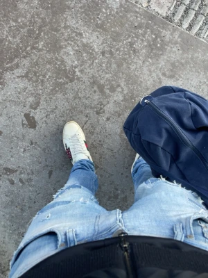 Vita sneakers från Gucci med röd/grön detalj - Säljer ett par klassiska vita sneakers från Gucci med den ikoniska röd-gröna randen på sidan och en liten broderad detalj i rött. Skorna har snörning och platt sula, perfekt för dig som vill ha en stilren och trendig look.