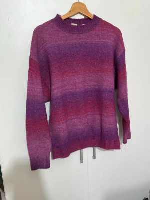 Lila och rosa stickad tröja från Levi’s - Mysig stickad tröja i lila och rosa toner med mjuka färgövergångar. Tröjan har rund halsringning, långa ärmar och ribbade muddar vid ärmslut och nederkant. Perfekt för dig som gillar färg och vill ha något bekvämt och snyggt. Tröjan är Limited edition och är slutsåld från alla butiker. Tröjan har inga skador alls, den är använd ett par gånger.