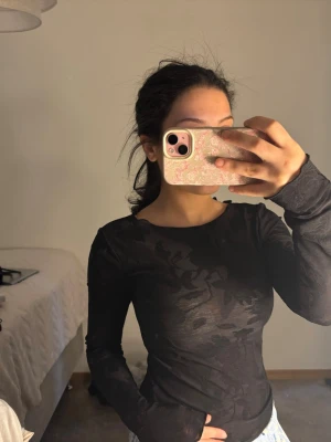 Svart blommig topp Gina Tricot - Snygg svart långärmad topp från Gina Tricot i transparent mesh med diskret blommigt mönster. Toppen har smala axelband med rosett-detaljer och sitter tight. Perfekt att styla med jeans eller kjol för en trendig look. 