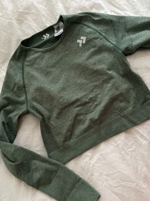 Grön långärmad crop top - Snygg grön långärmad crop top  med rund halsringning och diskret logga på bröstet. Tillverkad i ett stretchigt och mjukt material som passar perfekt till träning eller gym. Sömlös design för extra komfort.