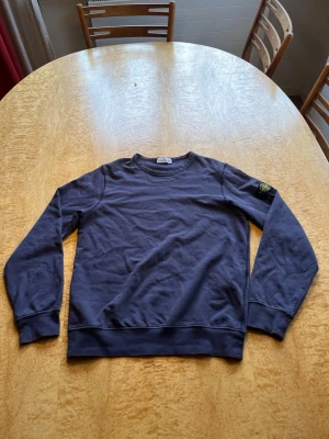 Lila blå sweatshirt från Stone Island - Snygg sweatshirt från Stone Island Junior med klassisk rund halsringning och ikonisk logopatch på vänster ärm. Tröjan är tillverkad i mjuk bomull och har ribbade muddar vid ärmslut och nederkant. Perfekt för en avslappnad och trendig look.